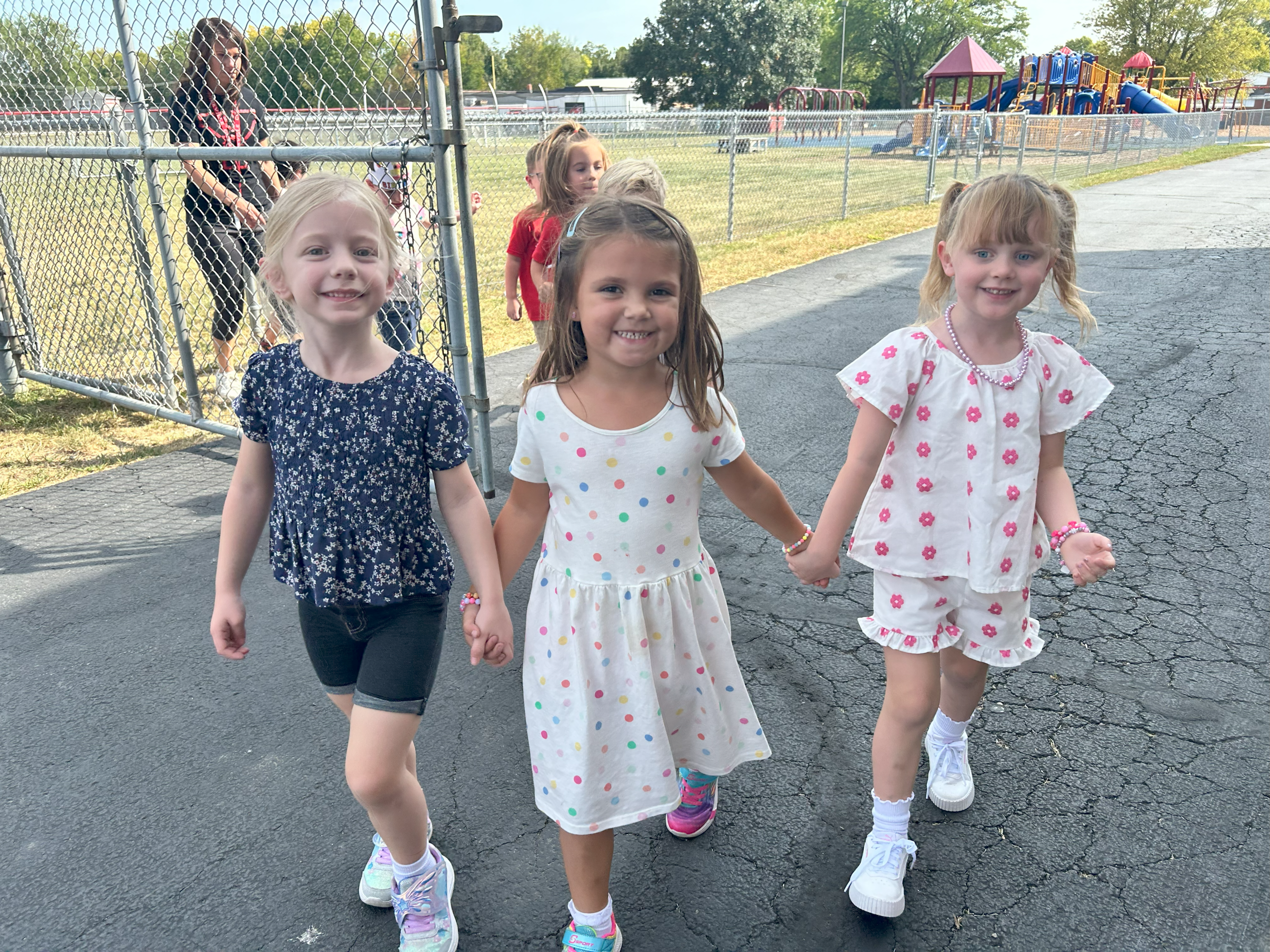 Three friends holding hands while walking outside. 
