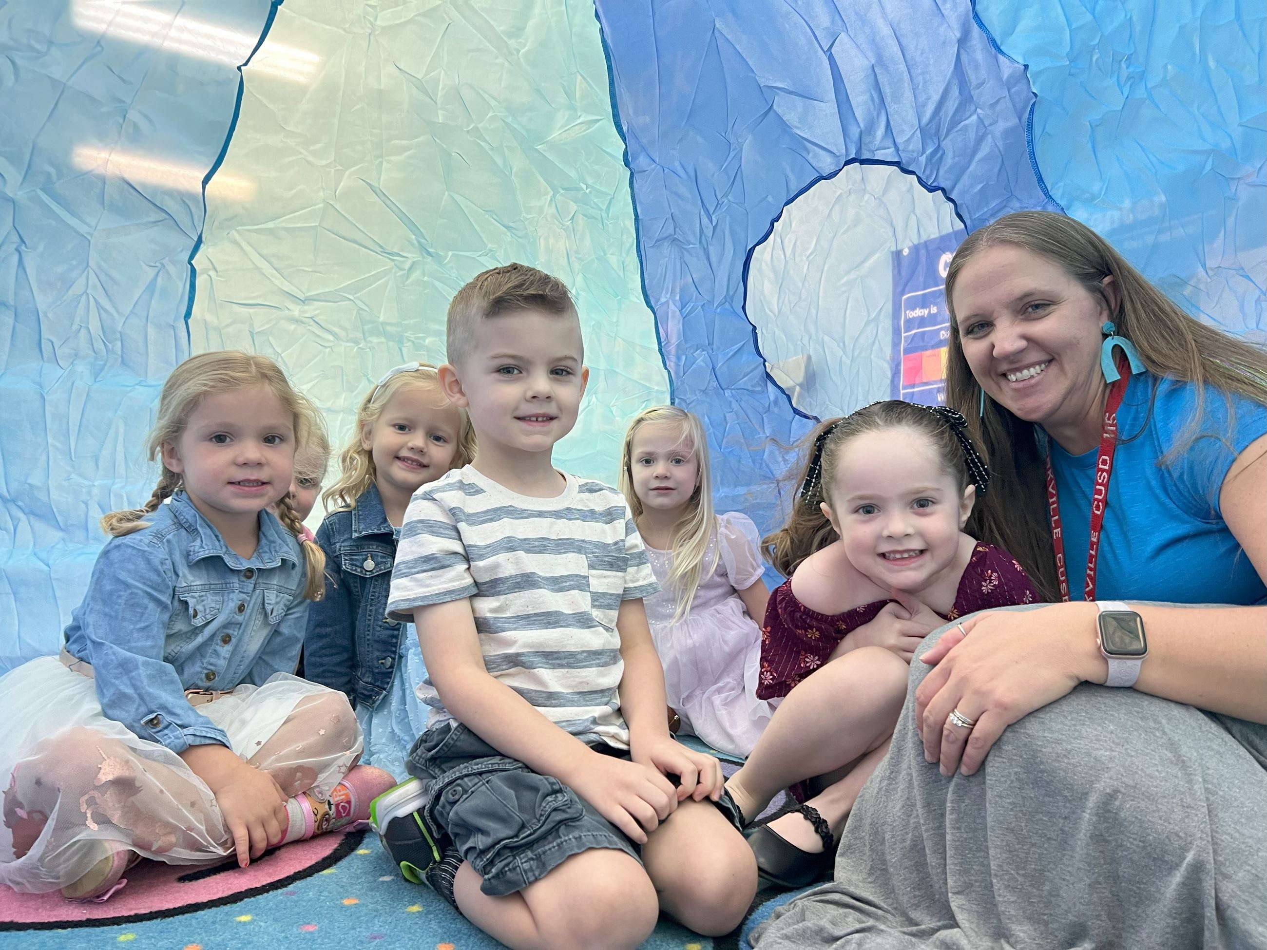 Students and teacher posing for a picture inside of an igloo.